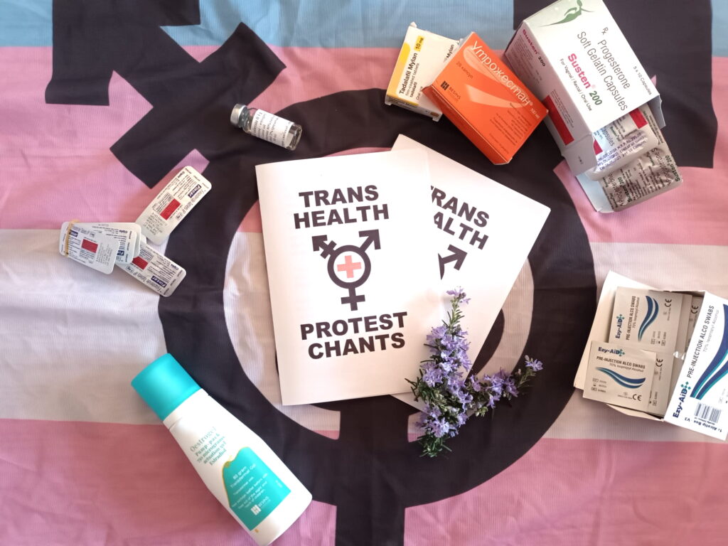 A zine lies on a trans flag, surrounded by medications